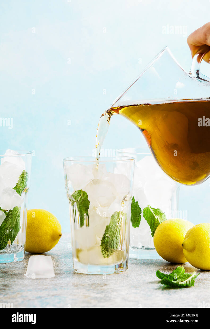 Versare dalla brocca tradizionale di tè freddo al limone con ghiaccio in bicchieri alti Foto Stock