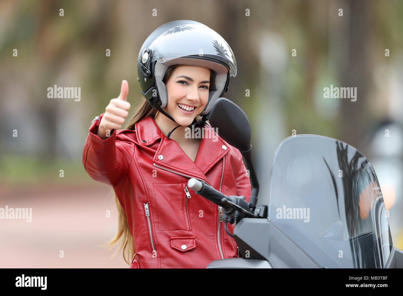 Felice biker guardando a voi con il pollice in su sulla sua moto all'aperto sulla strada Foto Stock