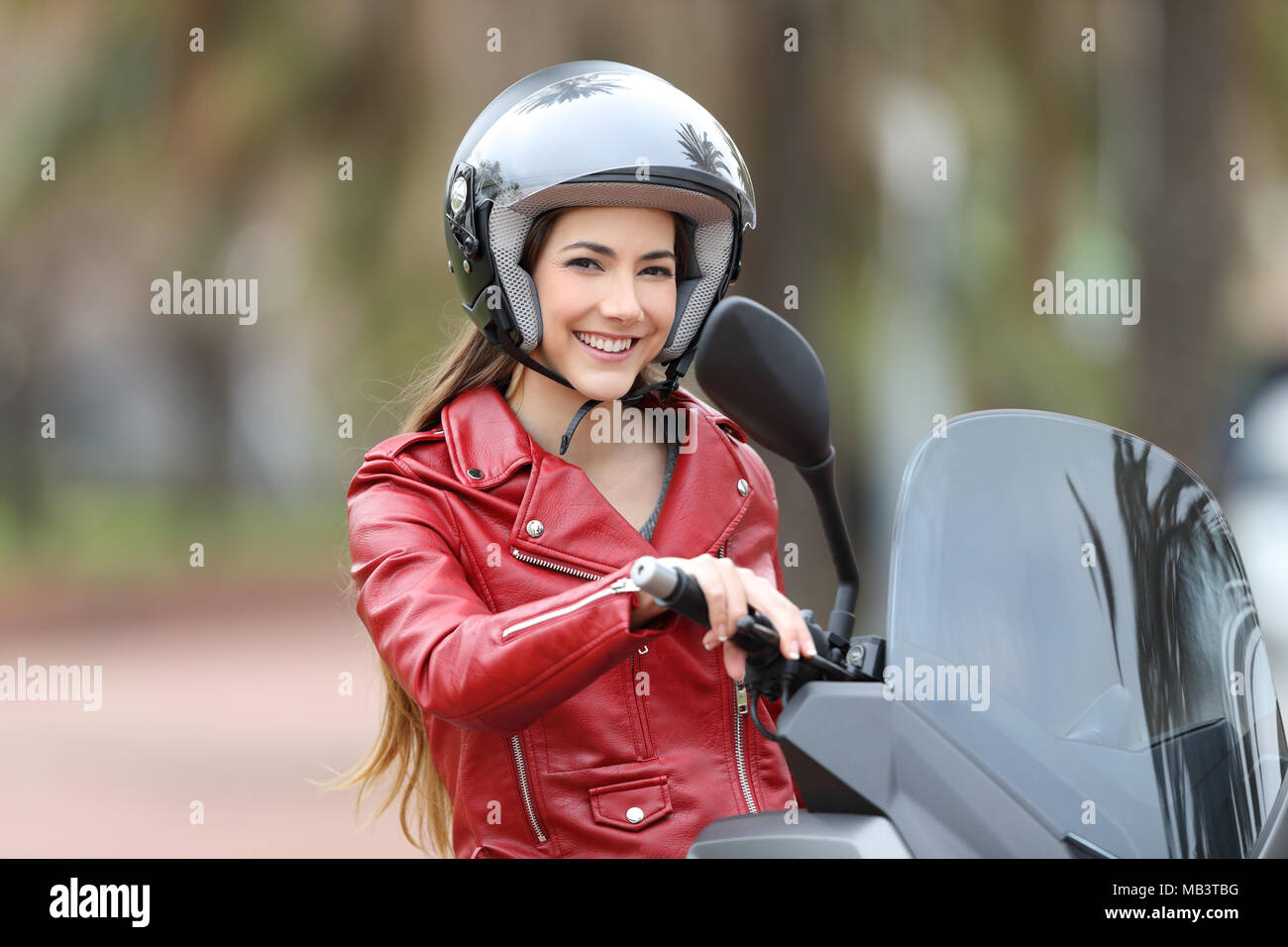 Felice biker che indossa un casco seduta sul suo moto guardando la fotocamera su strada Foto Stock