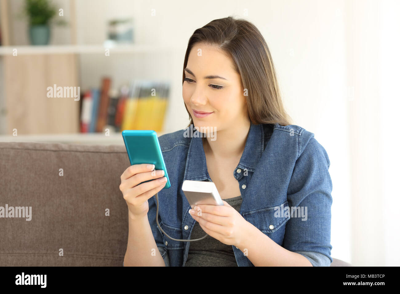 Ragazza carica di una smart phone con un caricabatterie portatile seduto su  un divano nel salotto di casa Foto stock - Alamy