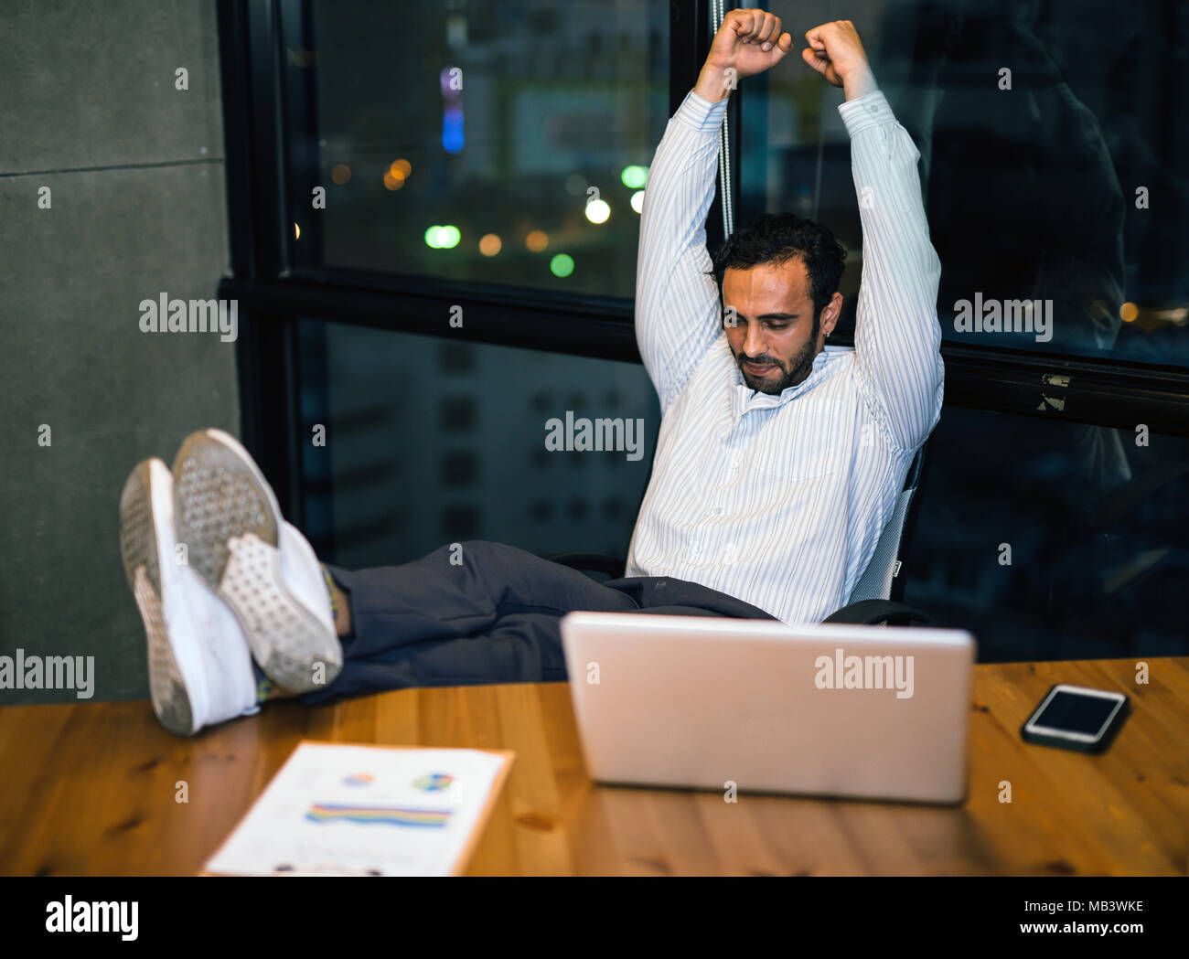 Rilassata fiducioso giovane impreditore seduta con le gambe sulla scrivania in ufficio il lavoro alla fine le ore di lavoro straordinario di notte la tabella del poggiapiedi Foto Stock