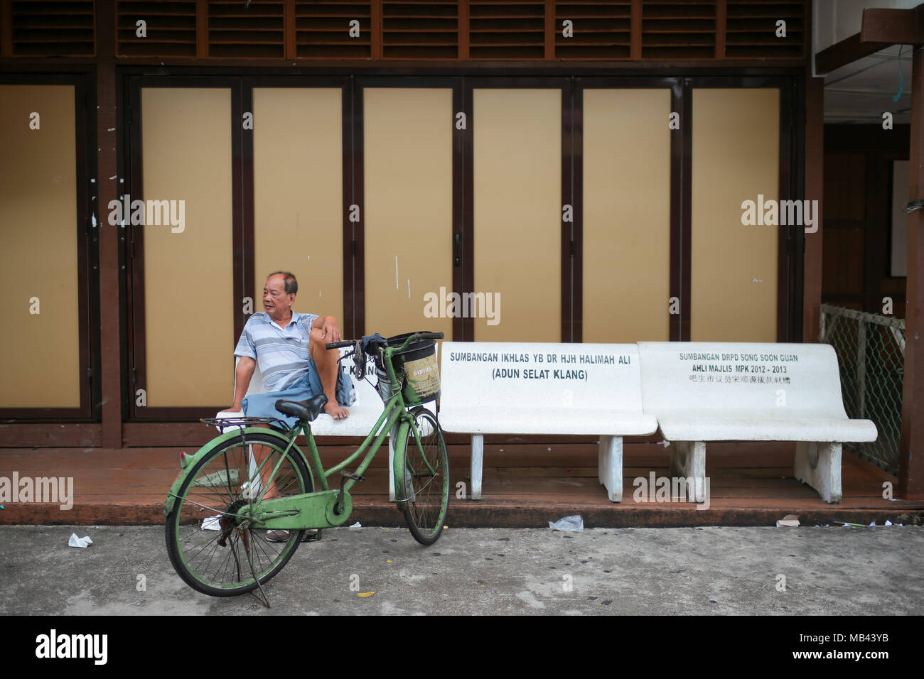 Un locale folk senior relax sul banco di fronte un negozio chiuso at Crab Island, Malaysia. Un famoso villaggio di pescatori in Malaysia. Foto Stock