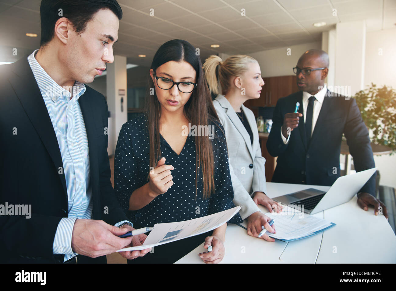 Gruppo diversificato di focalizzata corporate executives discutendo la documentazione insieme pur avendo un incontro a una tabella in un moderno edificio per uffici Foto Stock