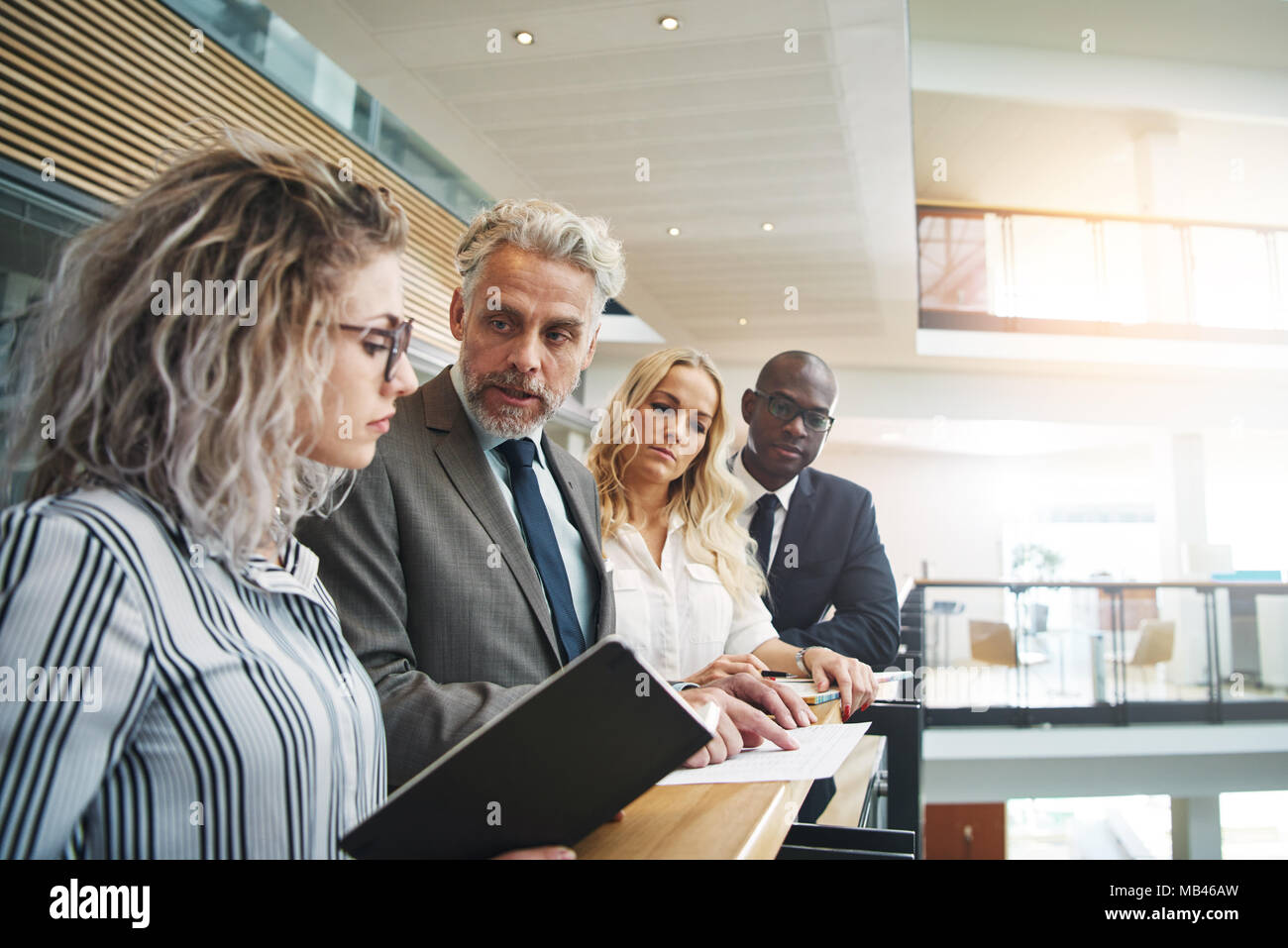 Gruppo diversificato di focalizzata corporate executives discutendo la documentazione insieme mentre in piedi presso la ringhiera in un corridoio di un moderno edificio per uffici Foto Stock
