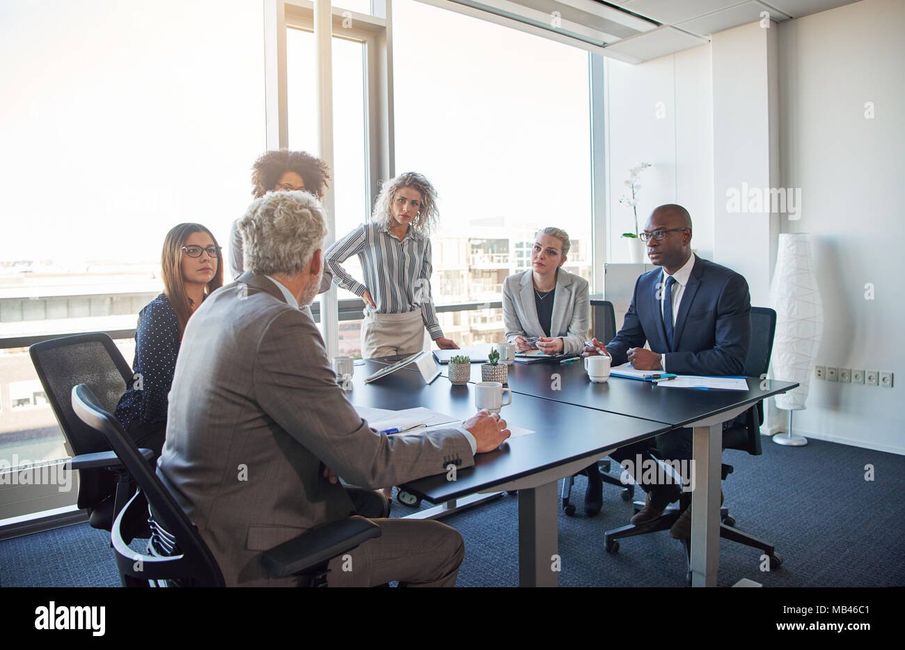 Diversi gruppi di dirigenti a discutere di affari insieme attorno ad un tavolo durante una riunione in un luminoso ufficio moderno Foto Stock