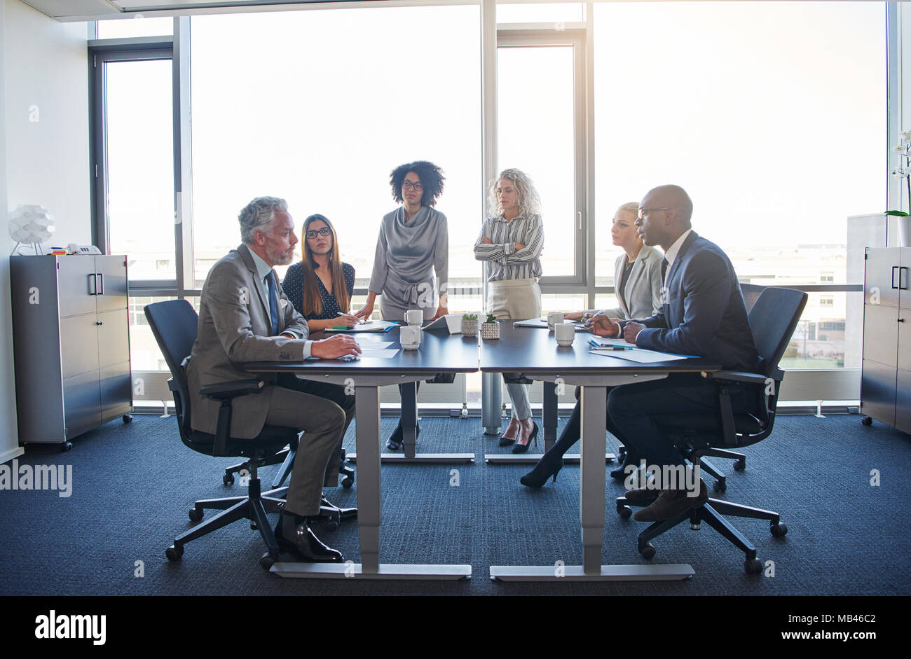 Gruppo diversificato di focalizzata corporate executives parlare insieme attorno ad un tavolo durante una riunione in un luminoso ufficio moderno Foto Stock