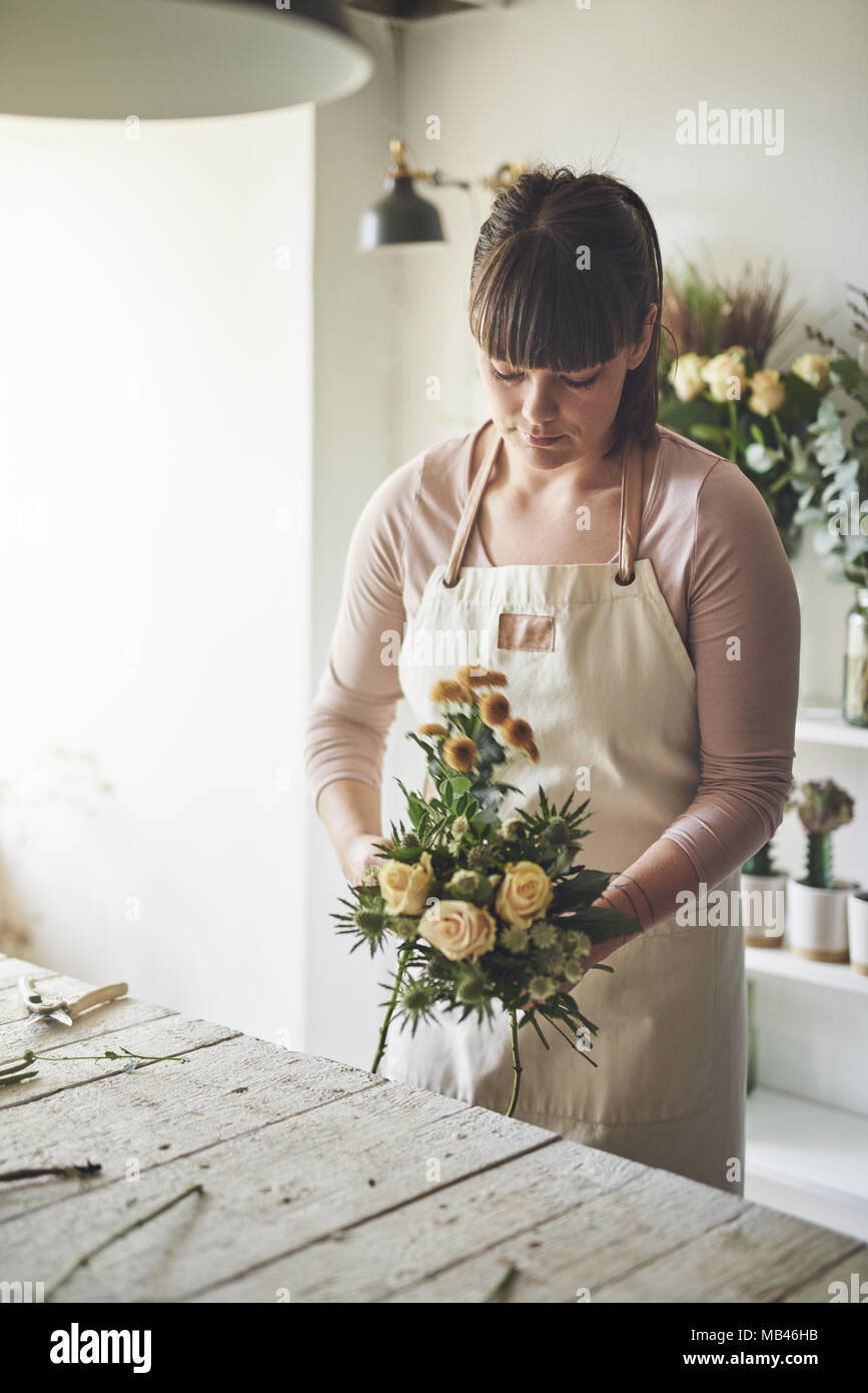 Fiorista femmina facendo un mazzo di rose mentre si lavora da solo a un tavolo nel suo negozio di fiori Foto Stock