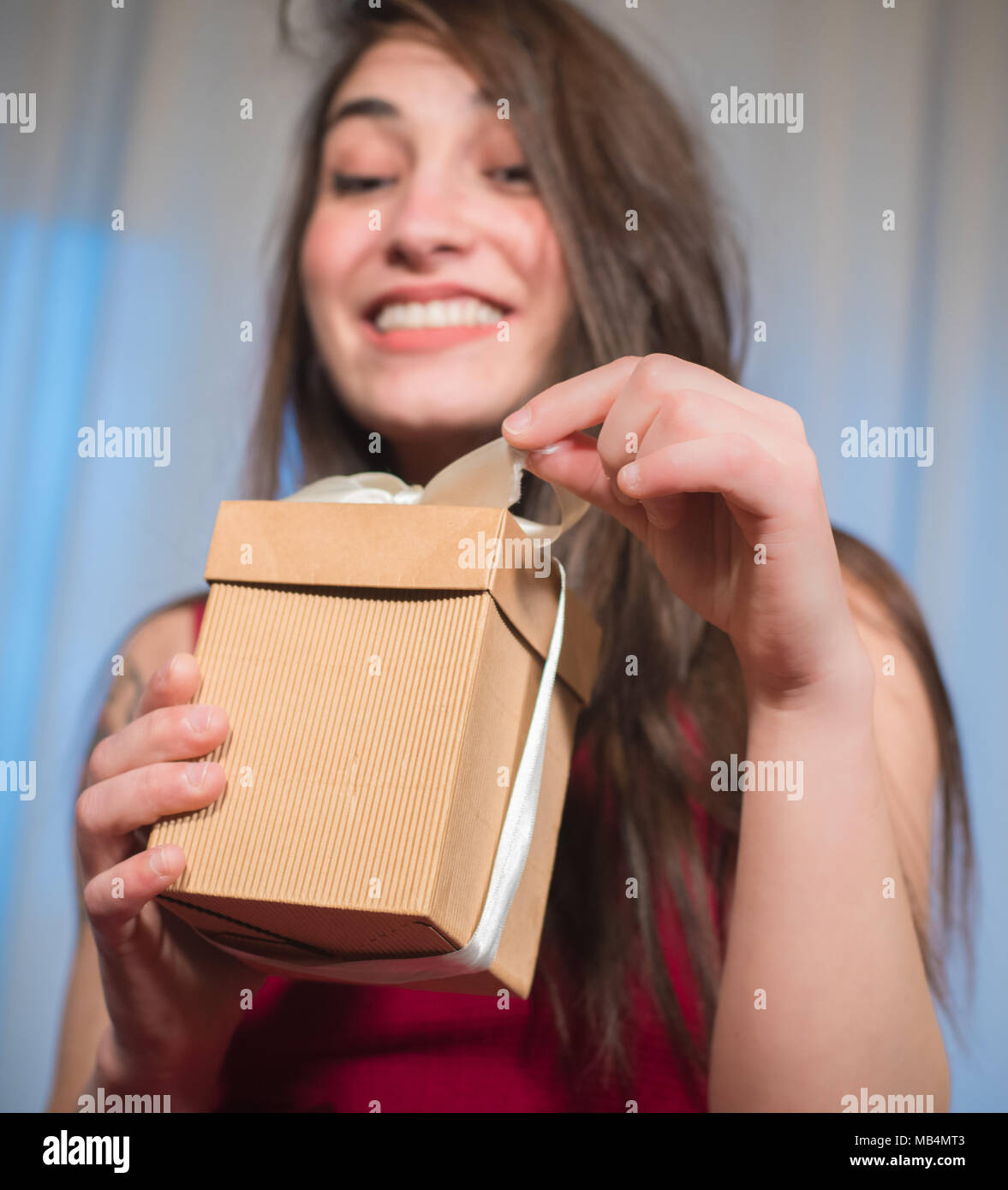 Stupiti donna felice apertura scatola regalo al di fuori della messa a fuoco in background eccitato e sorridente Foto Stock