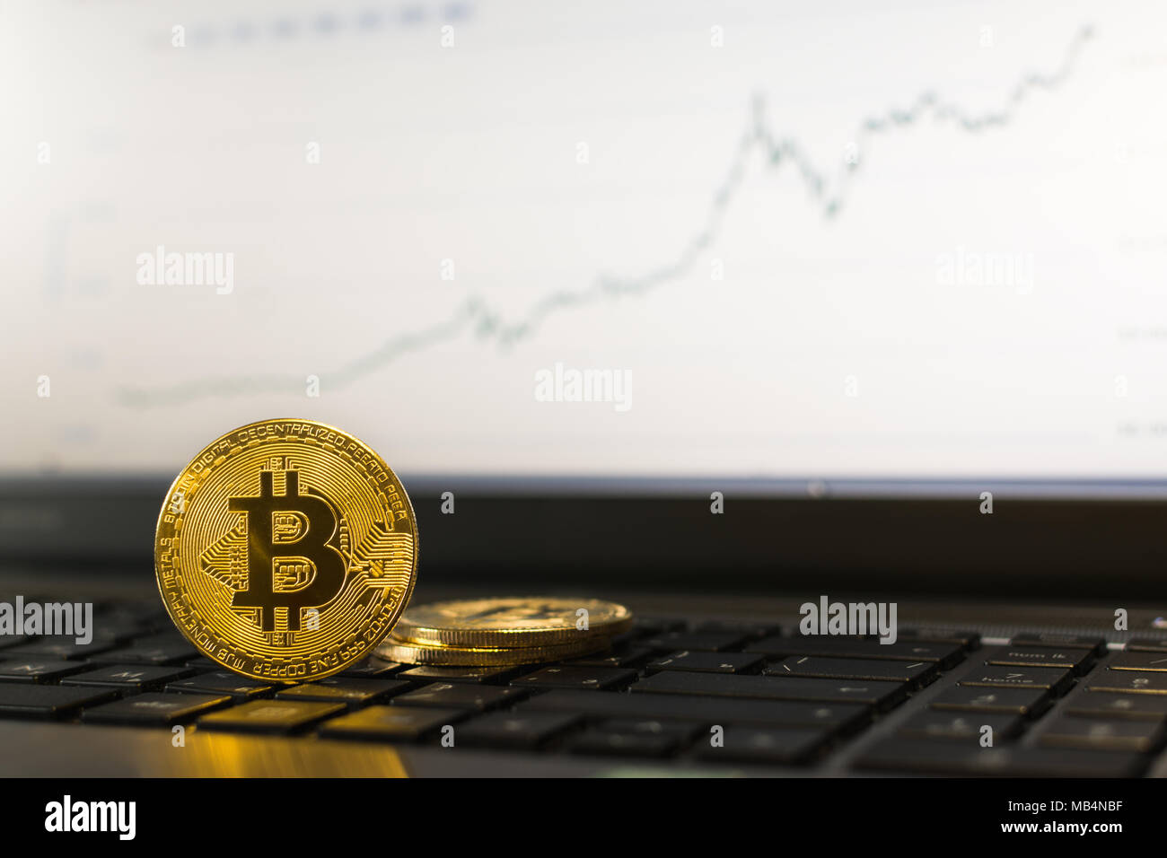 Bitcoin cryptocurrency coin in piedi su una tastiera portatile con ascendente grafico su sfondo sfocato Foto Stock