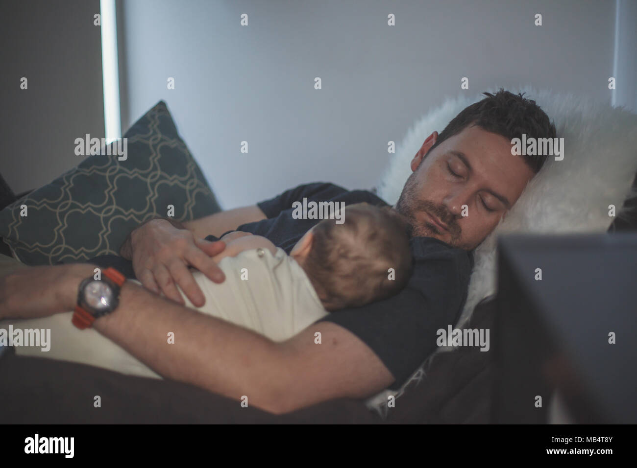 Giovane padre addormentato con il bambino tra le braccia Foto Stock