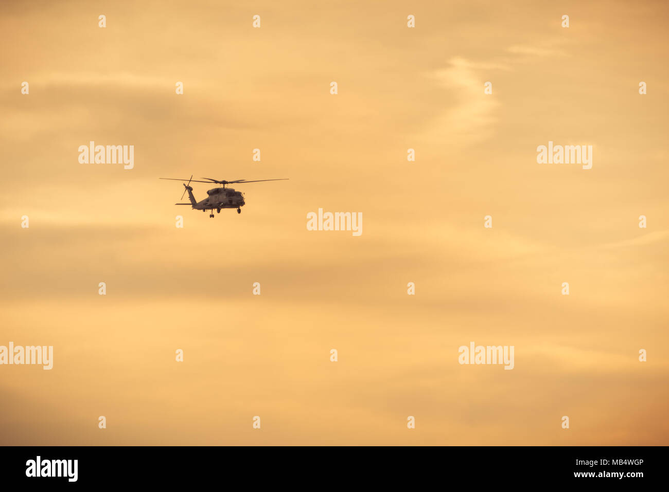 Un elicottero che vola contro amber sky al tramonto Foto Stock