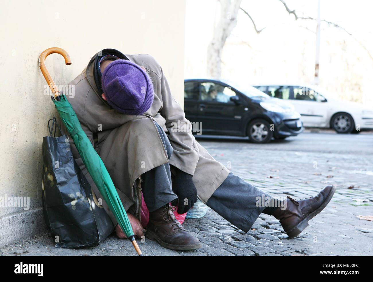 Senzatetto con hat, ombrello e borsa dormire in strada in una posizione in plastica Foto Stock