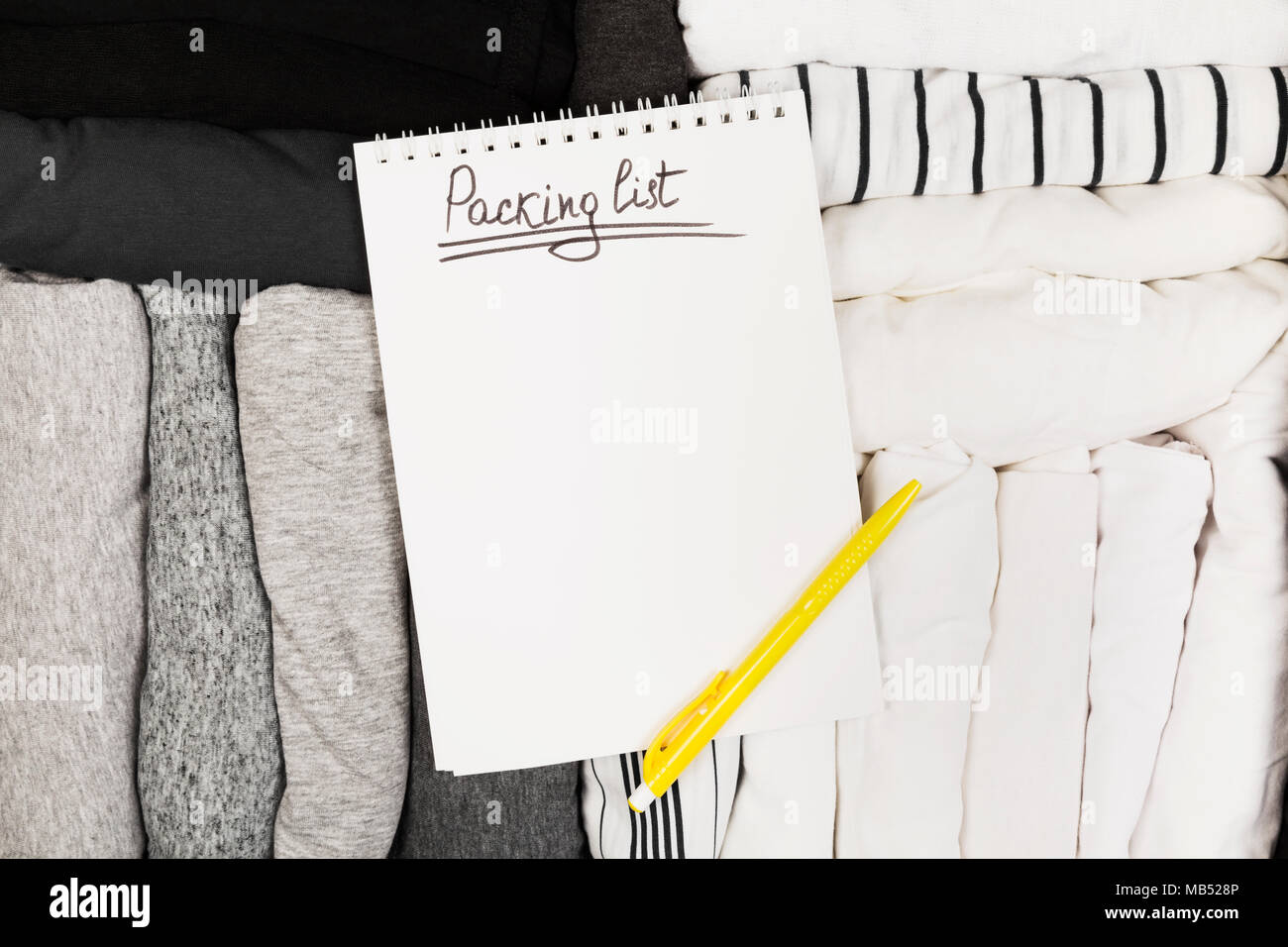 Confezionamento di abiti monocromatici in bianco e nero la valigia. Lista di imballaggio in bianco per notebook. Vista superiore, spazio di copia Foto Stock