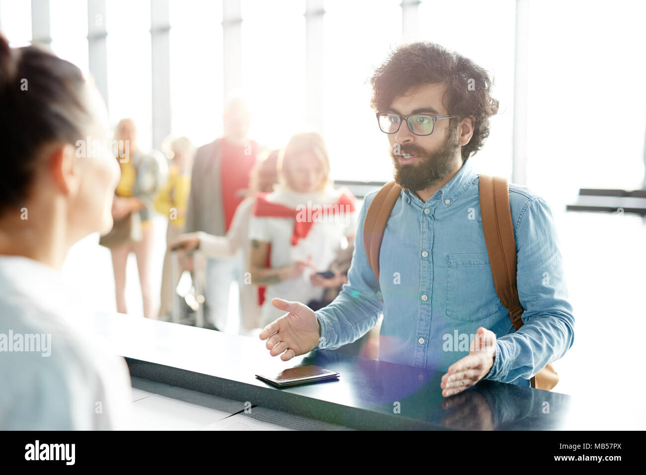 Indignato giovane uomo spiegare qualcosa al manager presso il banco di check-in durante il processo di registrazione Foto Stock