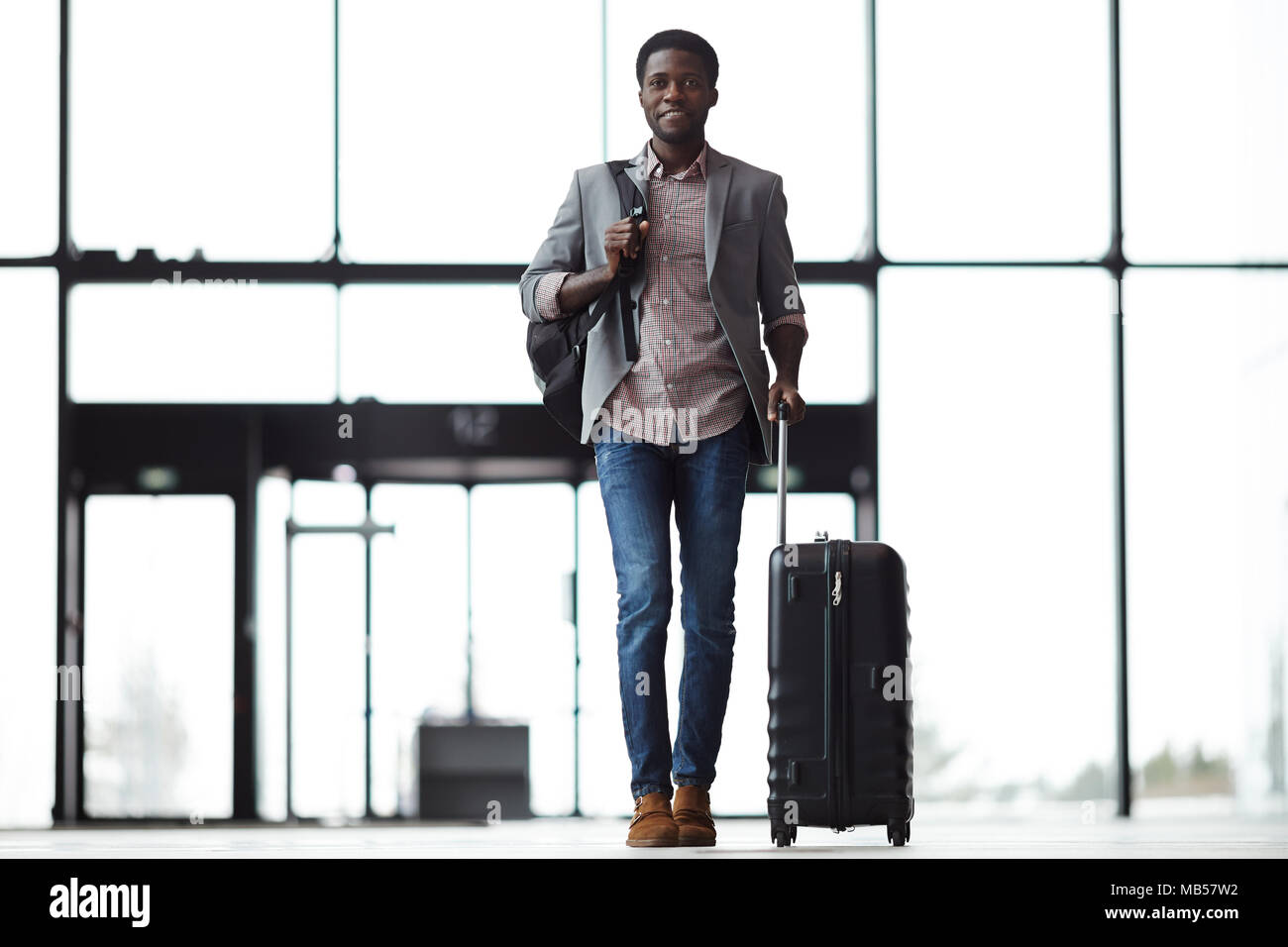 Felice giovane con zaino e valigia camminando lungo aeroporto al contatore di registrazione Foto Stock