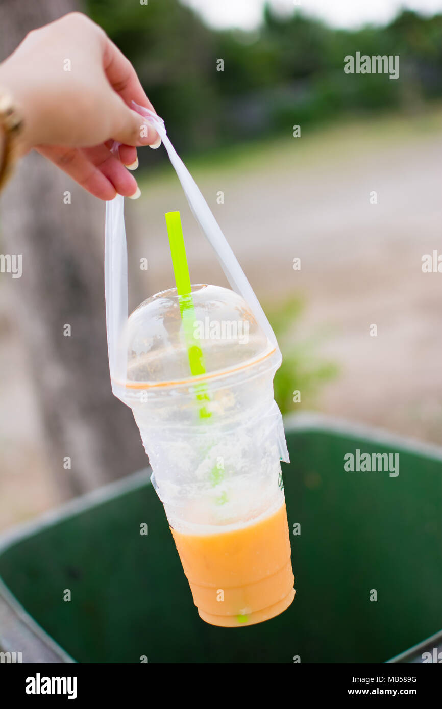 Non dimenticatevi di gettare il vostro cestino nel cestino. Donna di mano è di gettare il bicchiere vuoto per un verde bin, una tazza di plastica di Thai tè, Foto Stock
