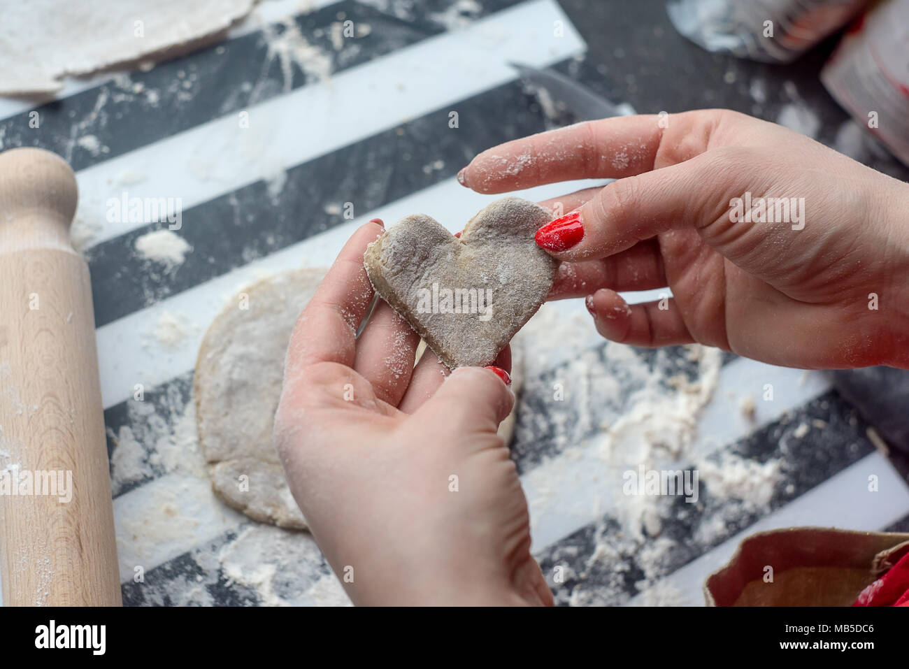 Donna cuore intagliato da impasto per i cookie, ha bel rosso chiodi. Foto Stock