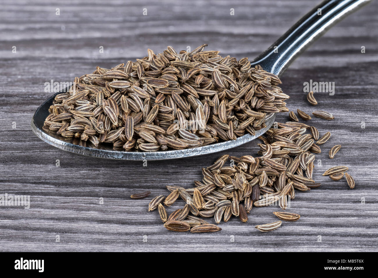 Close-up di aromatico caraways su legno. Carum carvi. Pila di secche semi di cumino sul cucchiaio inossidabile parzialmente versato sul marrone armonica di tonalità dello sfondo. Foto Stock