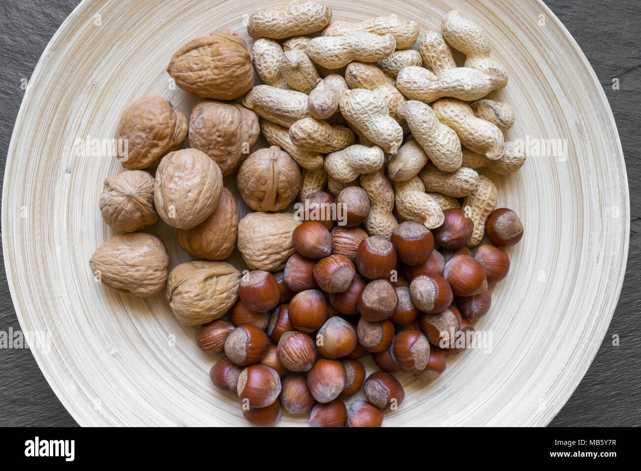 Arachidi, nocciole e noci con nutshells mix in bamboo naturale della piastra sulla pietra nera superficie di sfondo Foto Stock