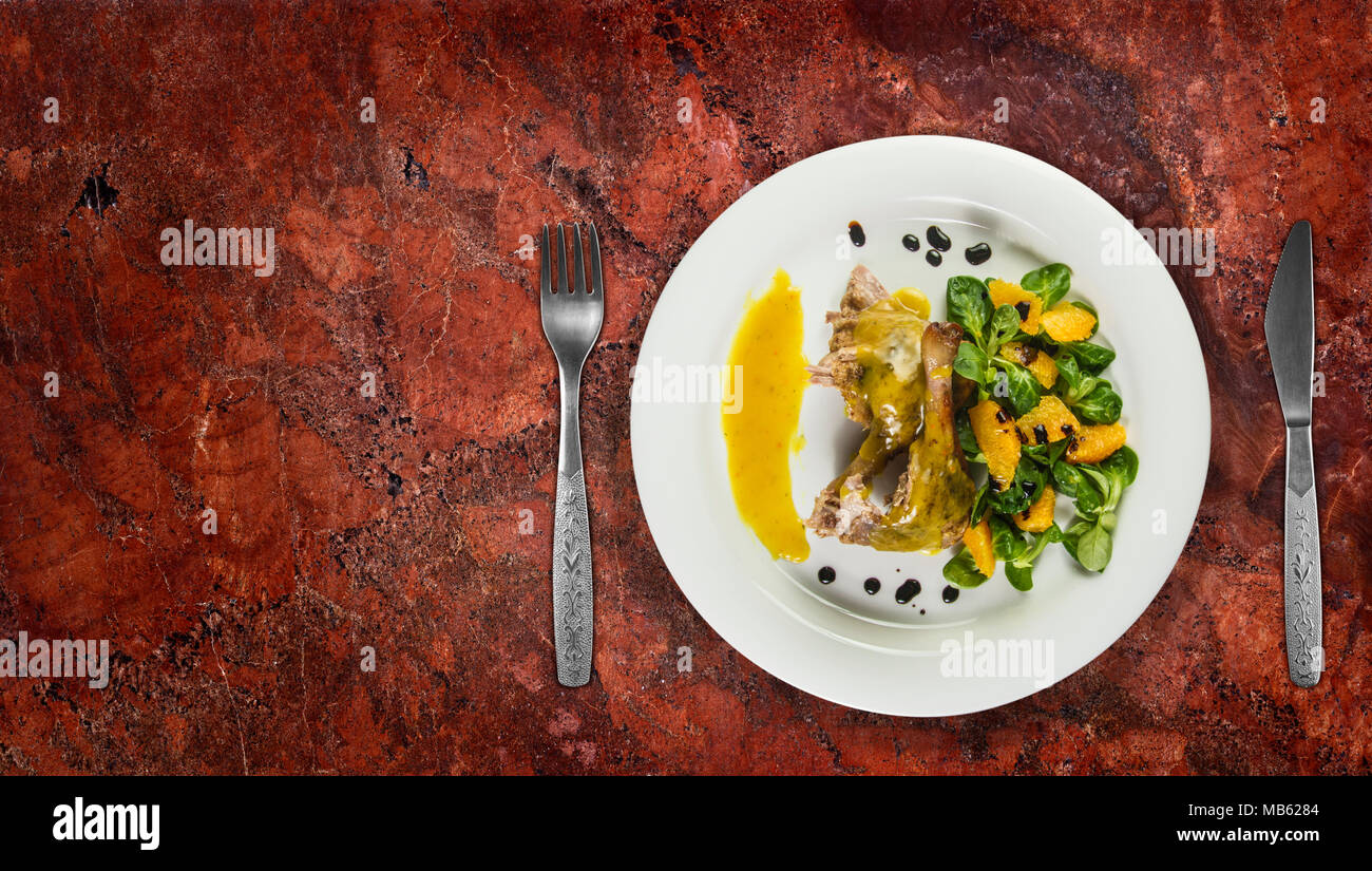 Gambe d'anatra con salsa di arancio e la valeriana con insalata di arance e aceto sulla piastra bianca sul ripiano in granito. Foto Stock