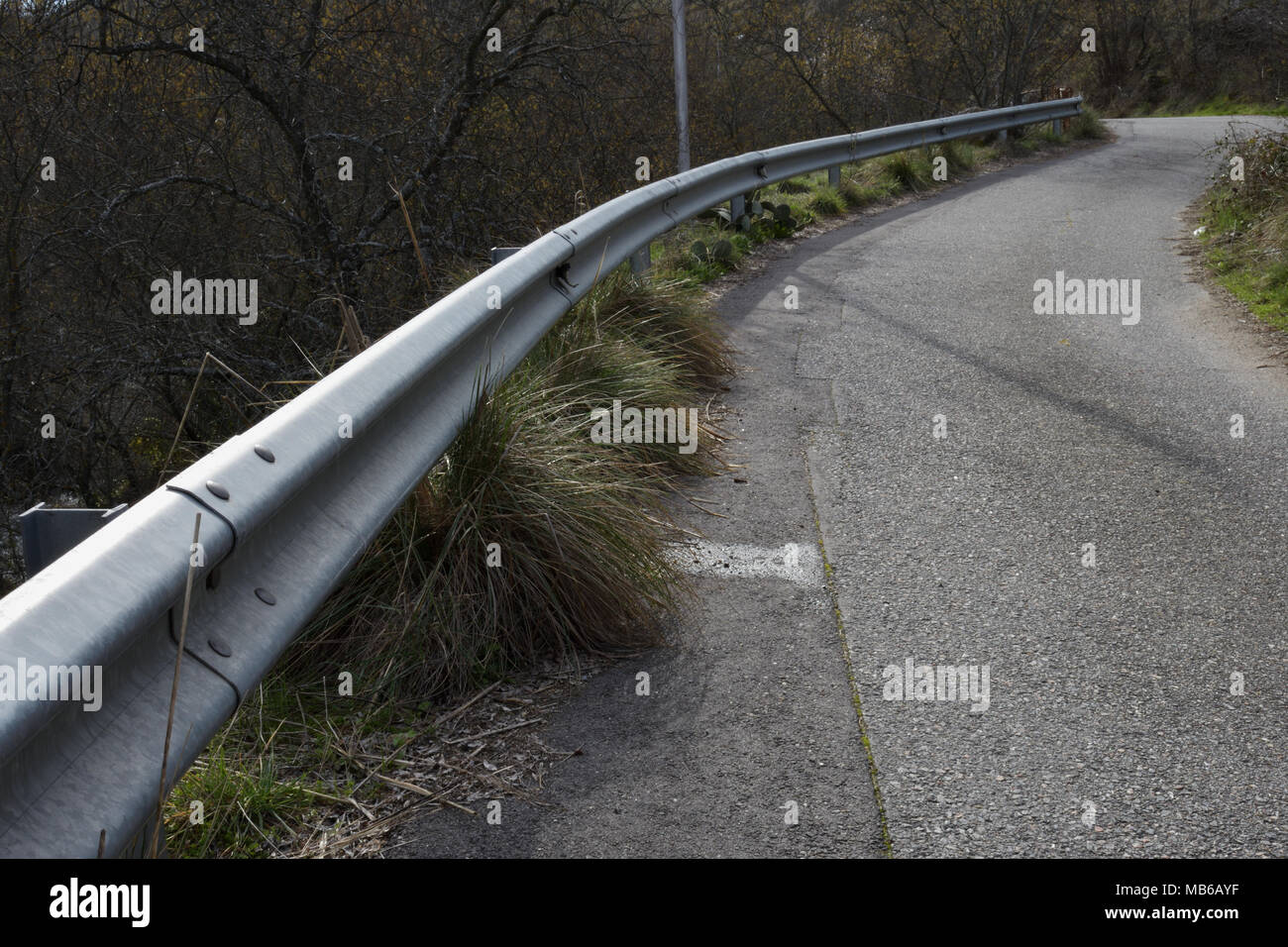 6575 patched stretta strada di montagna la curva con la barriera di sicurezza e macchia sul marciapiede Foto Stock