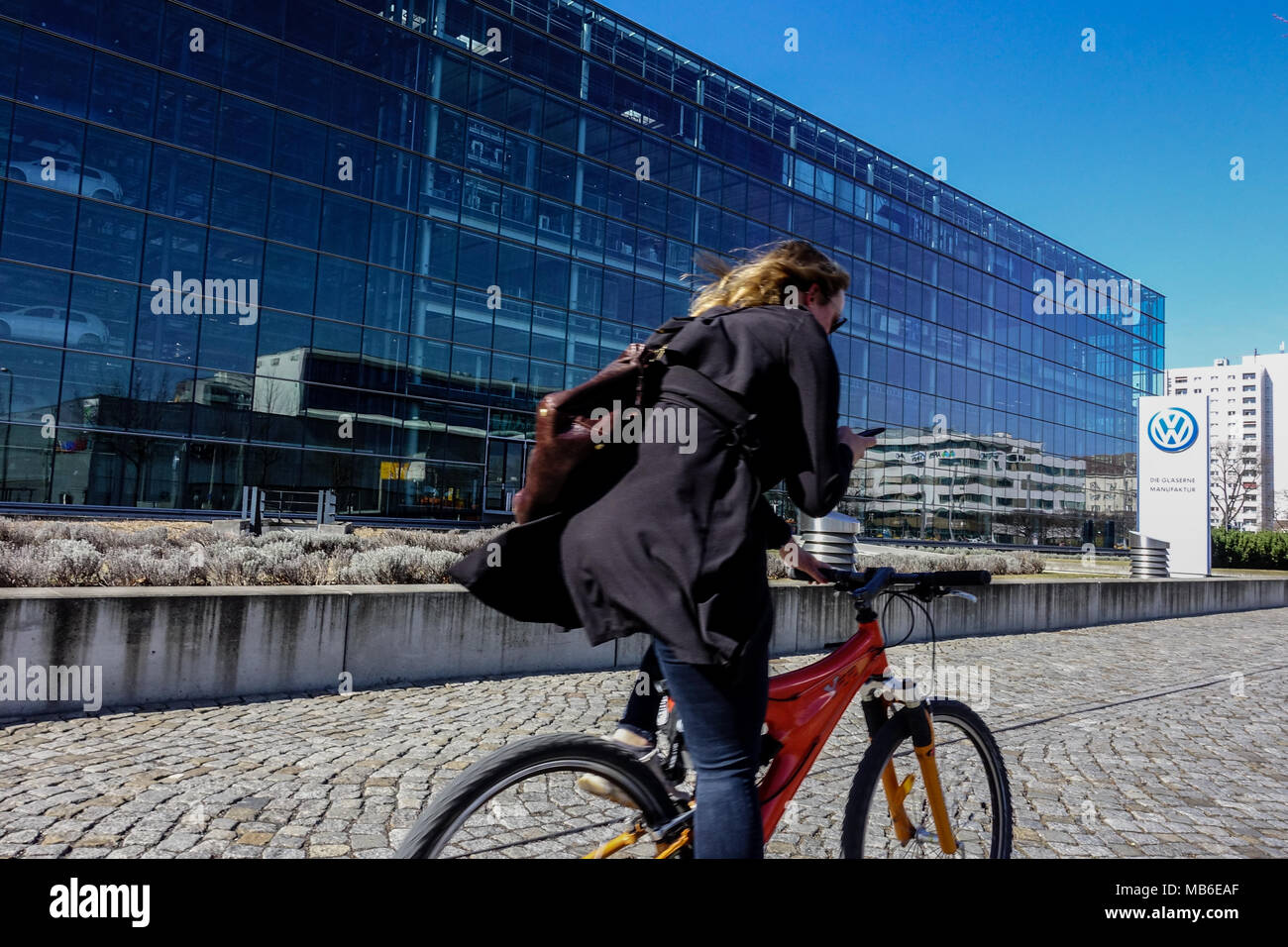 Una donna che usa un telefono cellulare mentre si guida una bicicletta alla fabbrica di automobili Volkswagen, Dresda, Sassonia, Germania strada bicicletta Europa Foto Stock