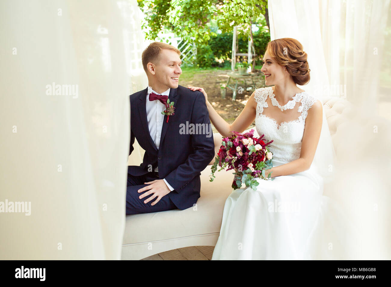 Happy sposi guardando ogni altro e seduto sul divano beige in posizione di parcheggio Foto Stock