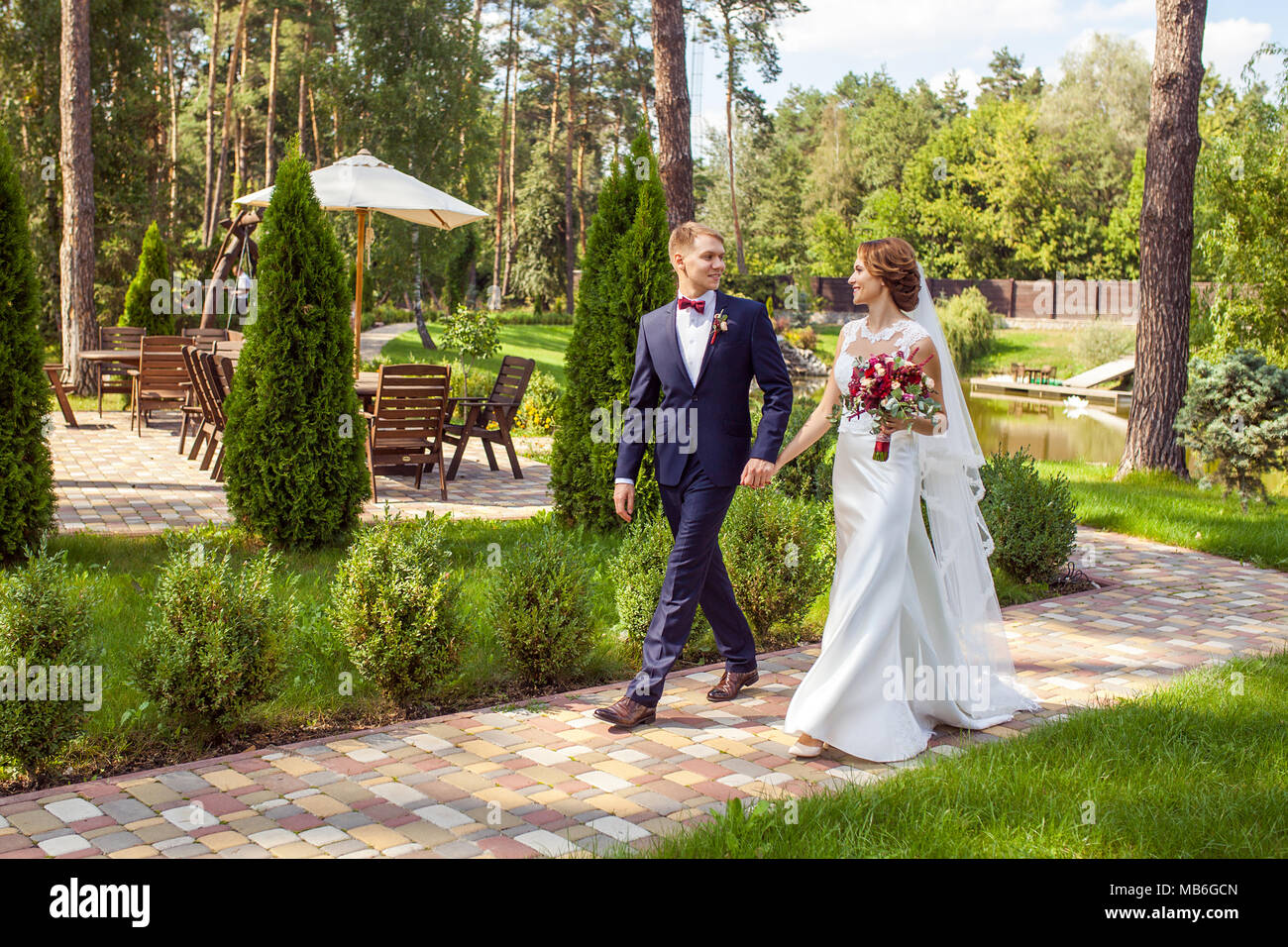 Happy sposi tenendo le mani e camminando sul marciapiede in estate park Foto Stock
