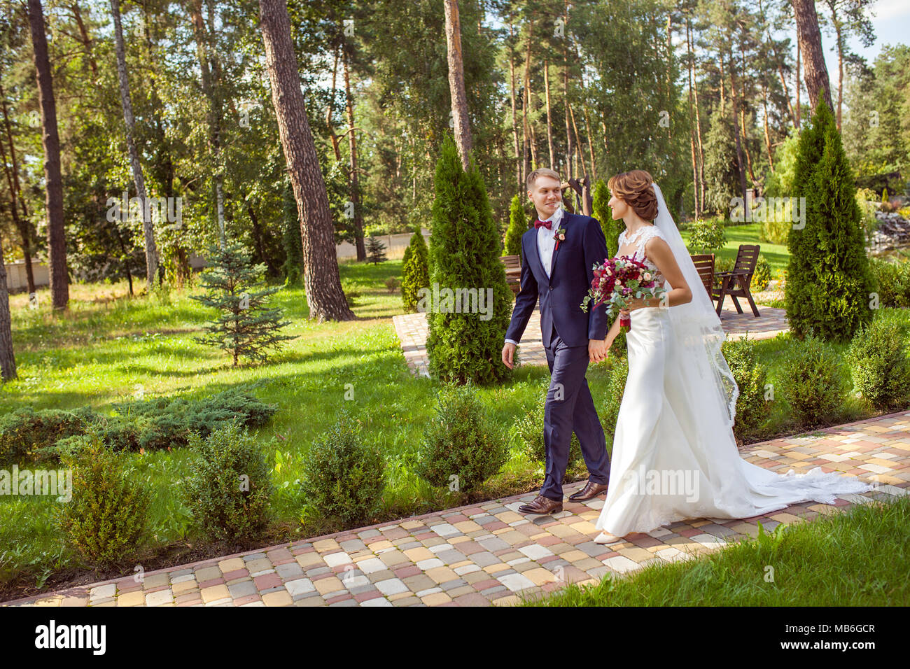 Happy sposi tenendo le mani e camminando sul marciapiede in estate park Foto Stock