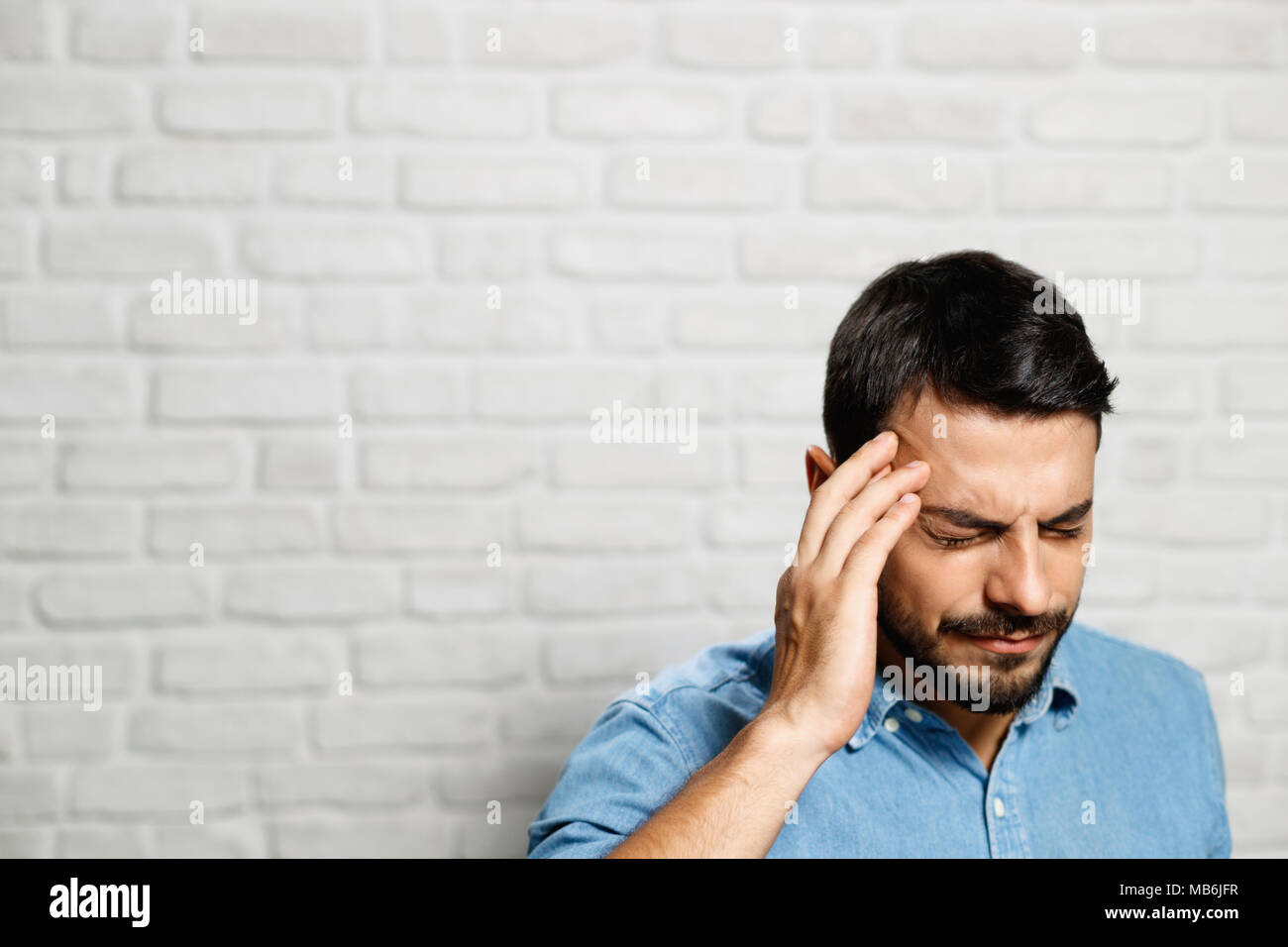 Le espressioni del viso dei giovani barba uomo su un muro di mattoni Foto Stock