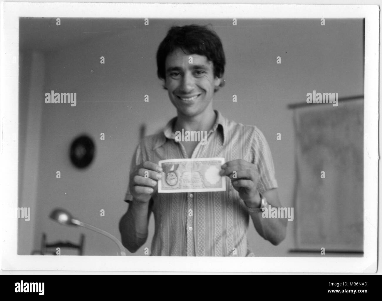 Giovane uomo sorridenti mantenendo un vecchio 100 Lire il disegno di legge italiano con le sue mani. Anni Settanta in bianco e nero. Italia office Foto Stock