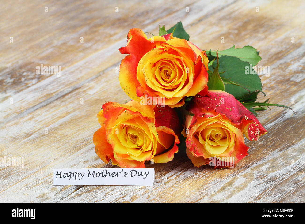 Felice Festa della mamma scheda con tre rose arancione coperta con glitter su una superficie di legno Foto Stock