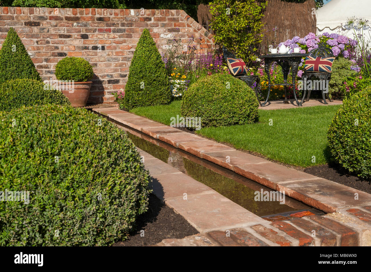 Acqua nel ruscello, ordinato prato, box sfere, parete & Tè per due nella soleggiata " è un riflesso della vita' show garden - RHS Flower Show, Tatton Park, Inghilterra, Regno Unito. Foto Stock