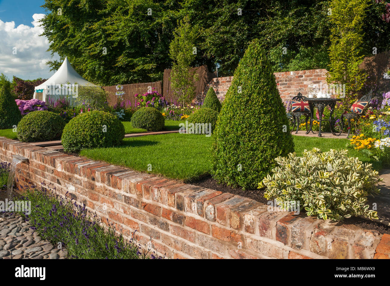 Cascata di acqua dal ruscello, prato, box sfere & Tè per due nella soleggiata " è un riflesso della vita' show garden - RHS Flower Show, Tatton Park, Inghilterra, Regno Unito. Foto Stock