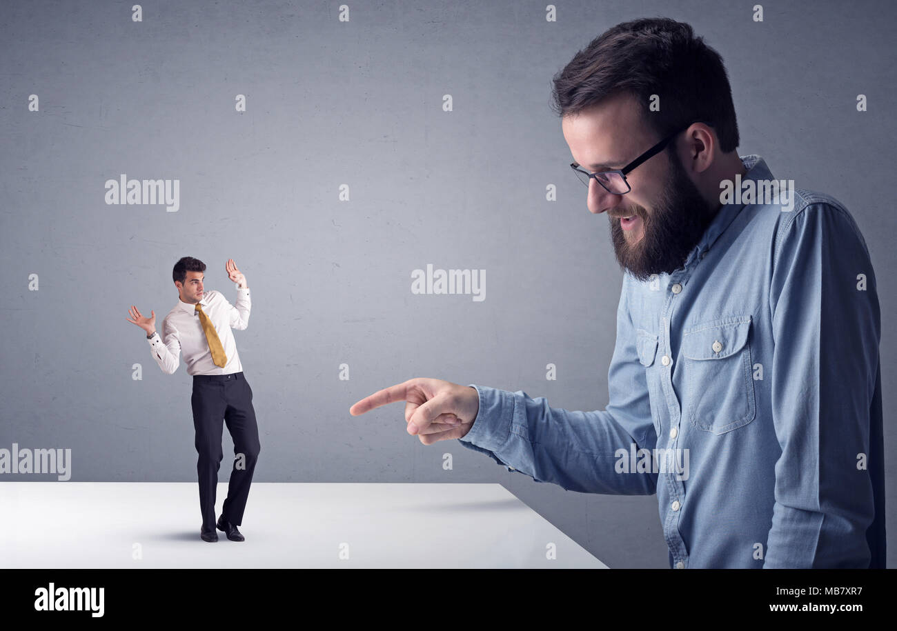 Giovane imprenditore professionale essendo arrabbiato con un altro imprenditore in miniatura di fronte a uno sfondo grigio Foto Stock