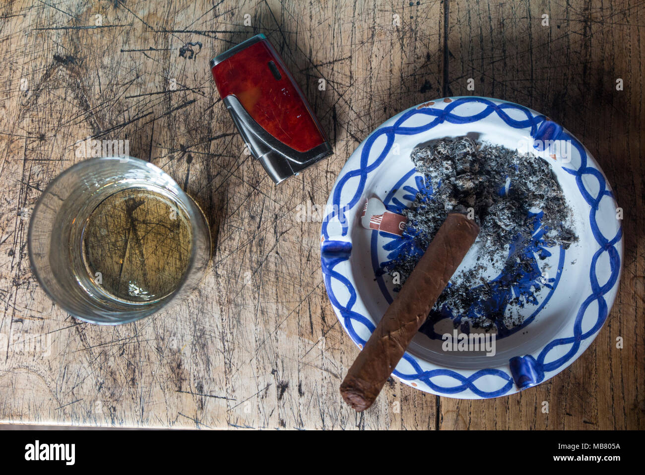 Un bicchiere di whisky, un sigaro, un accendisigari e un posacenere su una tabella presa da sopra Foto Stock