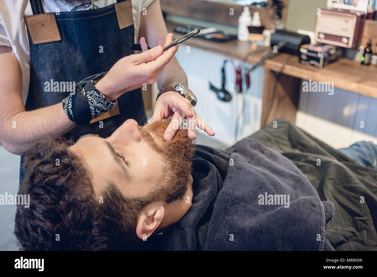 Barbuto giovane uomo pronto per la rasatura nel salone di parrucchiere di un esperto barbiere Foto Stock