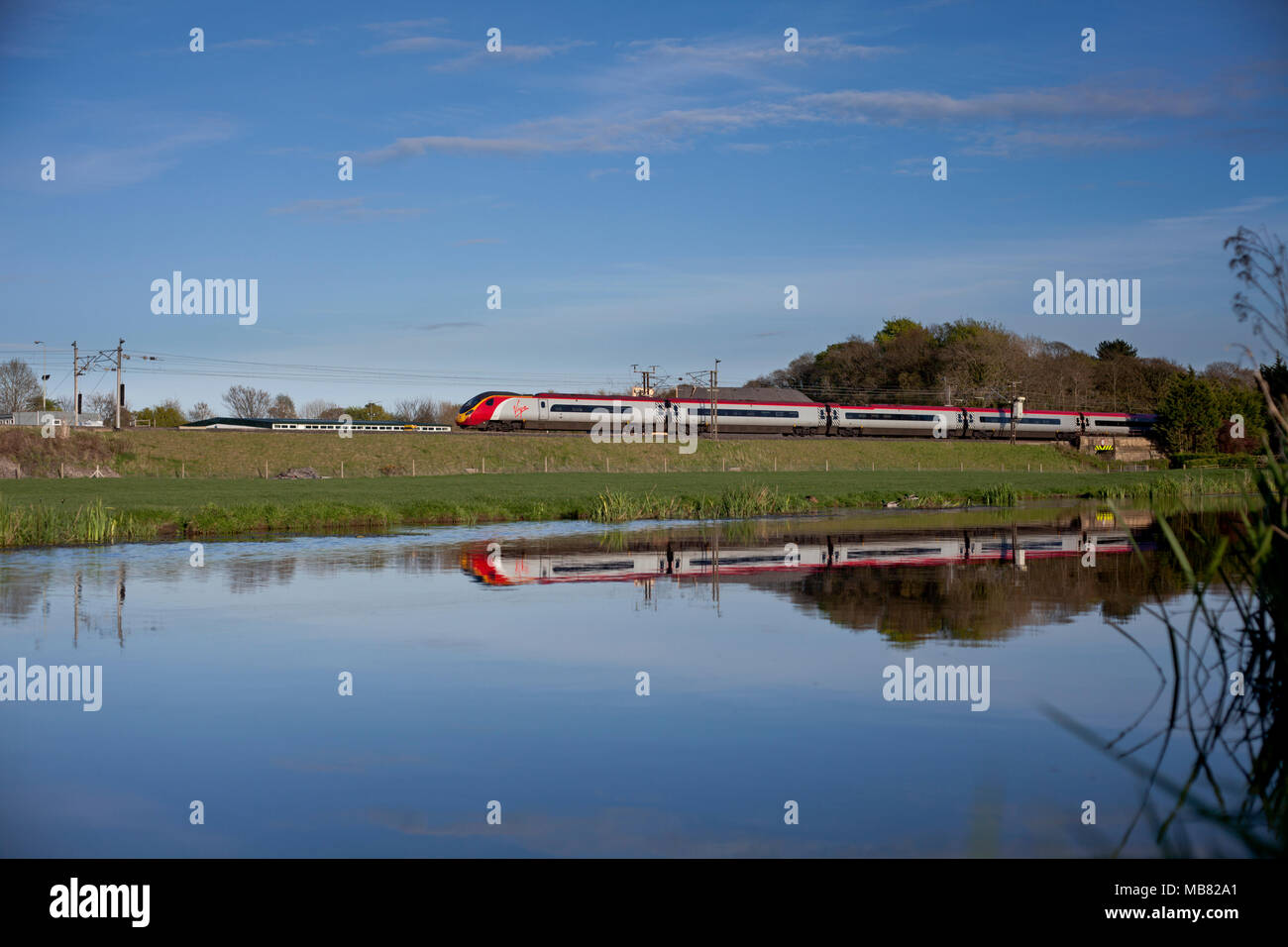 Un Virgin Trains west coast treno pendolino riflessa in Lancaster canal sulla linea principale della costa occidentale a Catterall a nord di Preston Foto Stock