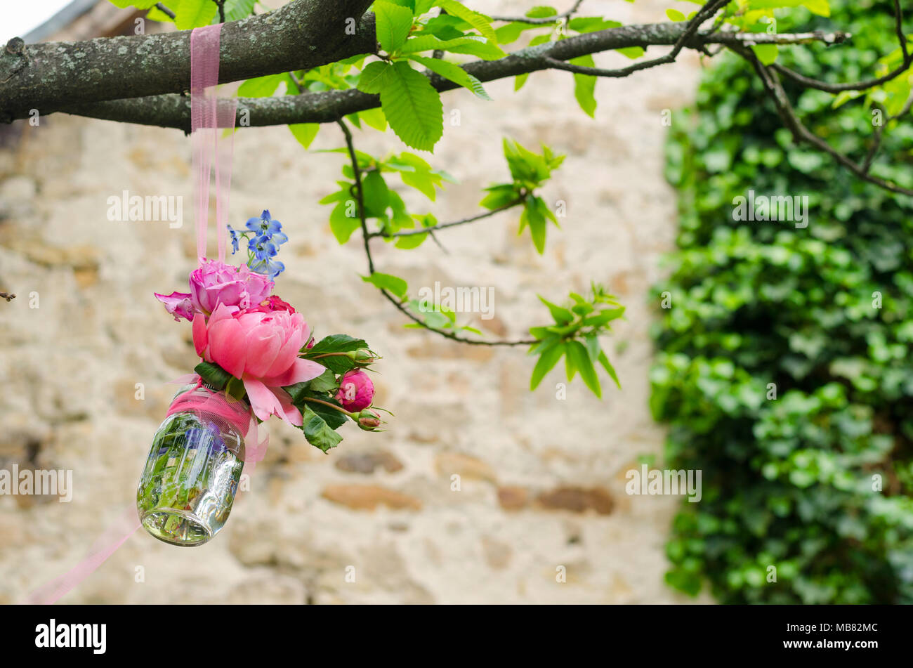 Improvvisato decorativo in vetro vaso di fiori pendenti da un albero di fronte a un vecchio muro di pietra in un parco Foto Stock