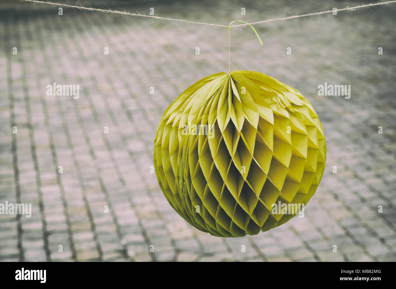 Orange carta decorativa sfera a nido d'ape appeso davanti di un grungy pavimentazione di pietra. vintage effetti di filtro. Foto Stock
