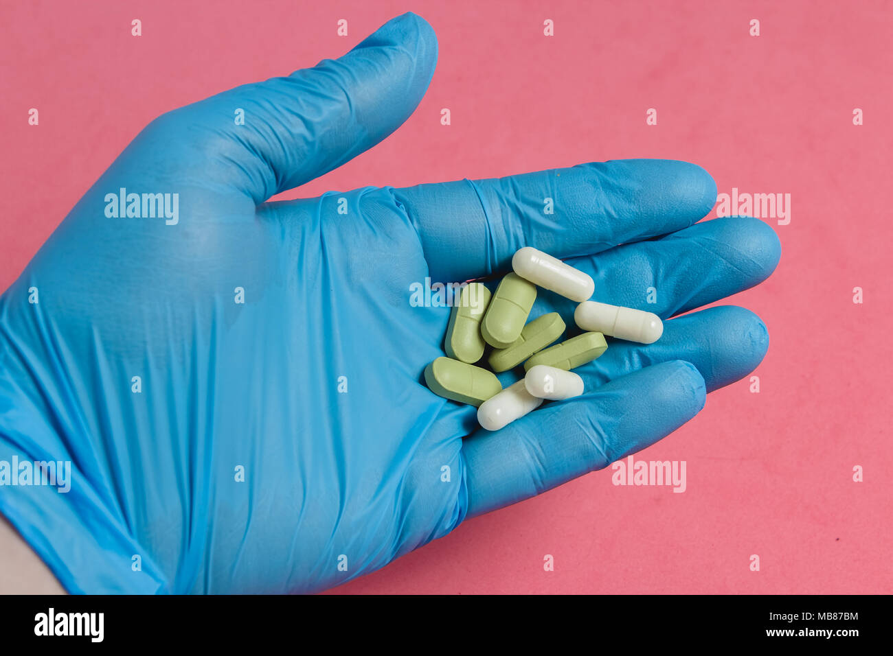 Assortimento di pillole, compresse e capsule a portata di mano nel guanto blu contro sfondo rosa. Foto Stock
