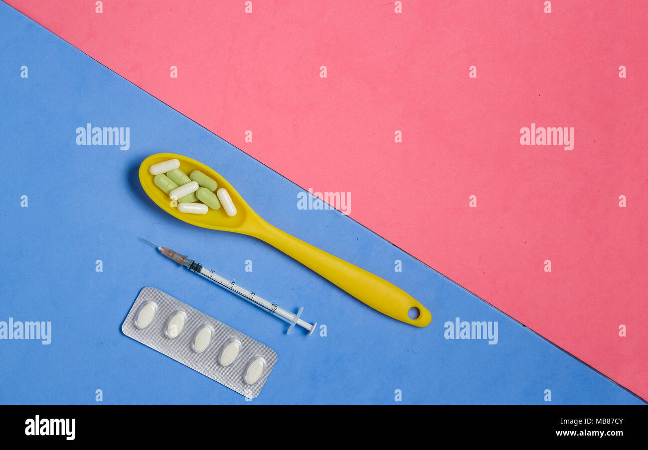 Pillole e capsule in giallo cucchiaio, siringa su sfondo blu con Copyspace rosa. Foto Stock