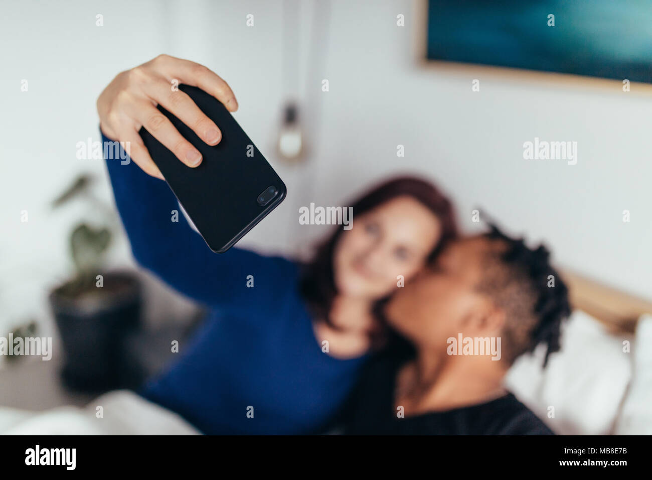 Giovane giacente insieme sul letto e rendendo selfie con il telefono cellulare. Focus su smart phone in mano di donna. Foto Stock