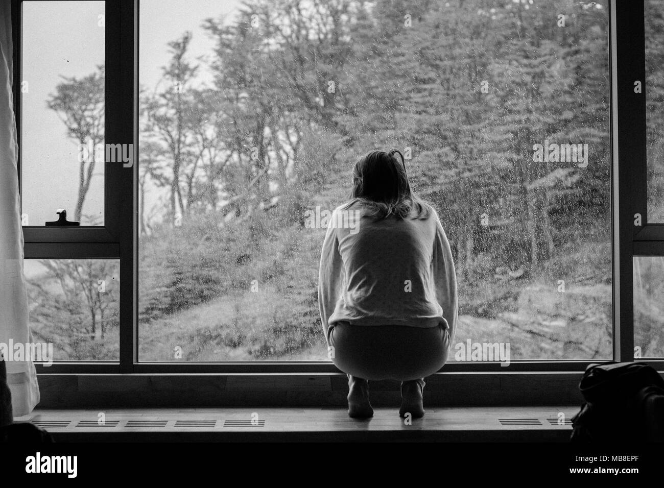 Giovane donna che guarda fuori dalla finestra al sensore pioggia Foto stock  - Alamy