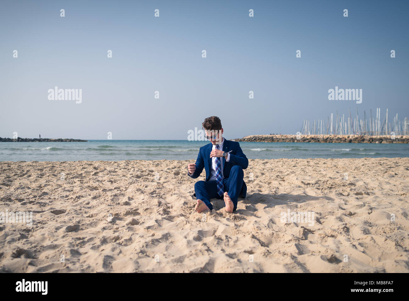 Funny manager in elegante abito si rilassa sulla spiaggia. Elegante ragazzo si siede sulla sabbia e di avere il tempo di riposo Foto Stock