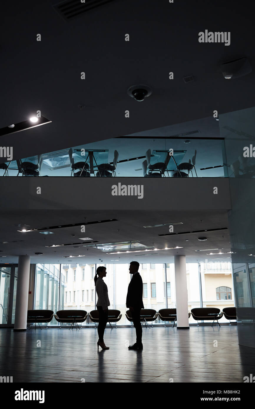 Interno della spaziosa lobby di office con finestre panoramiche, sagome ob business persone in piedi di fronte a ogni altro Foto Stock