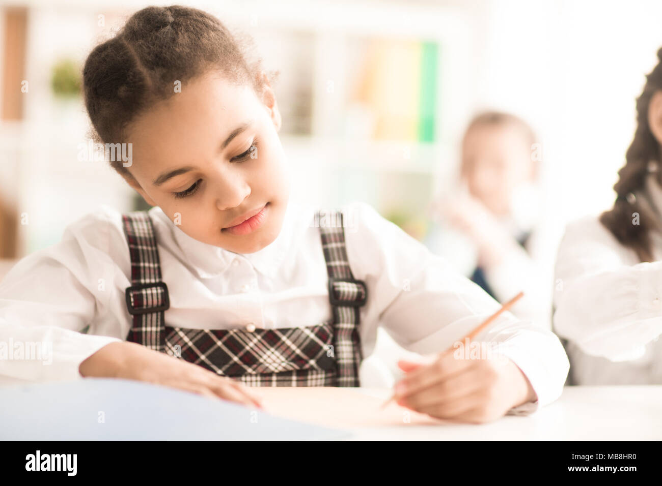 Grave schoolgirl seduto e iscritto al tavolo a scuola Foto Stock