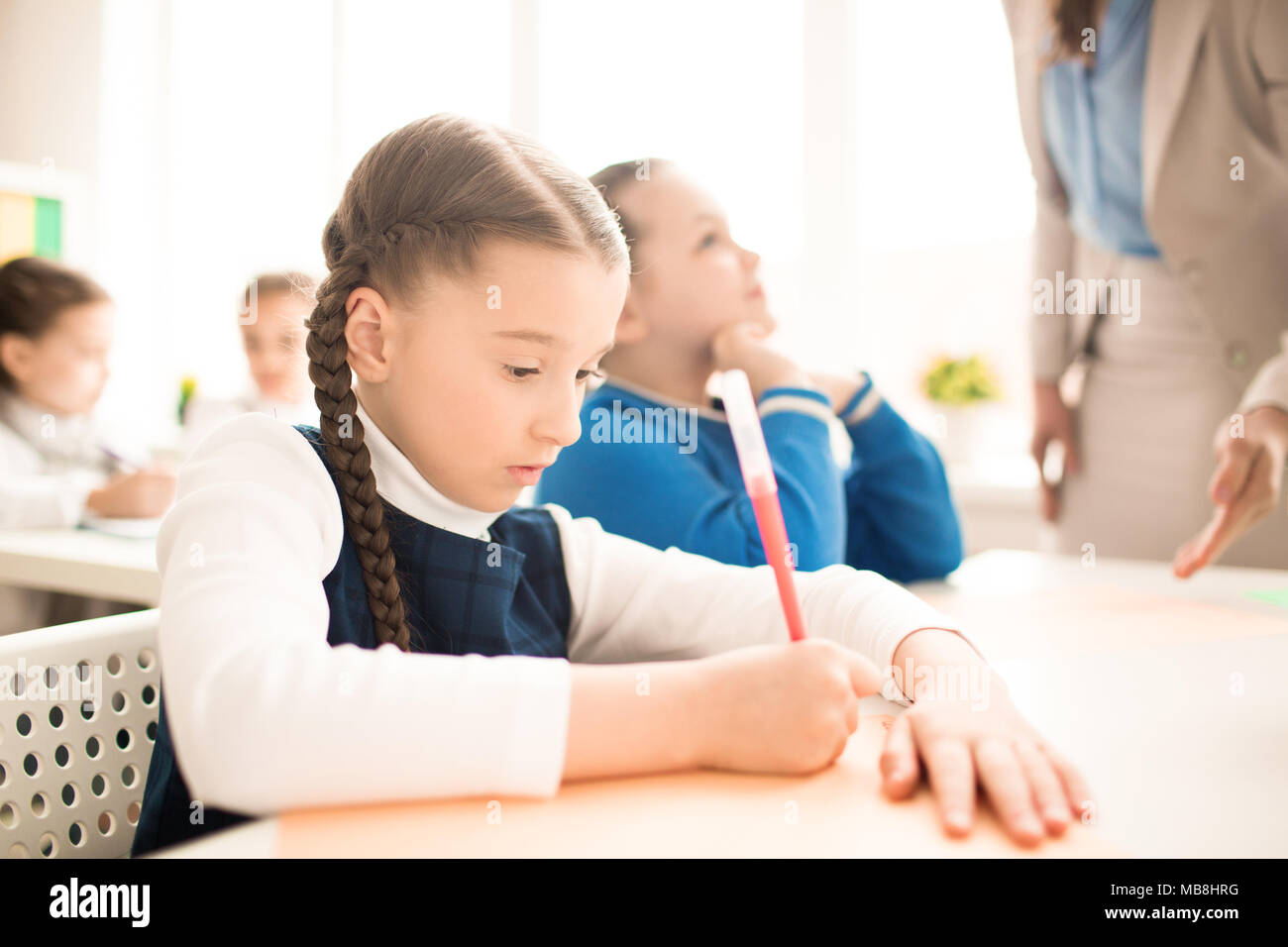 Grave schoolgirl facendo compito al tavolo in aula Foto Stock