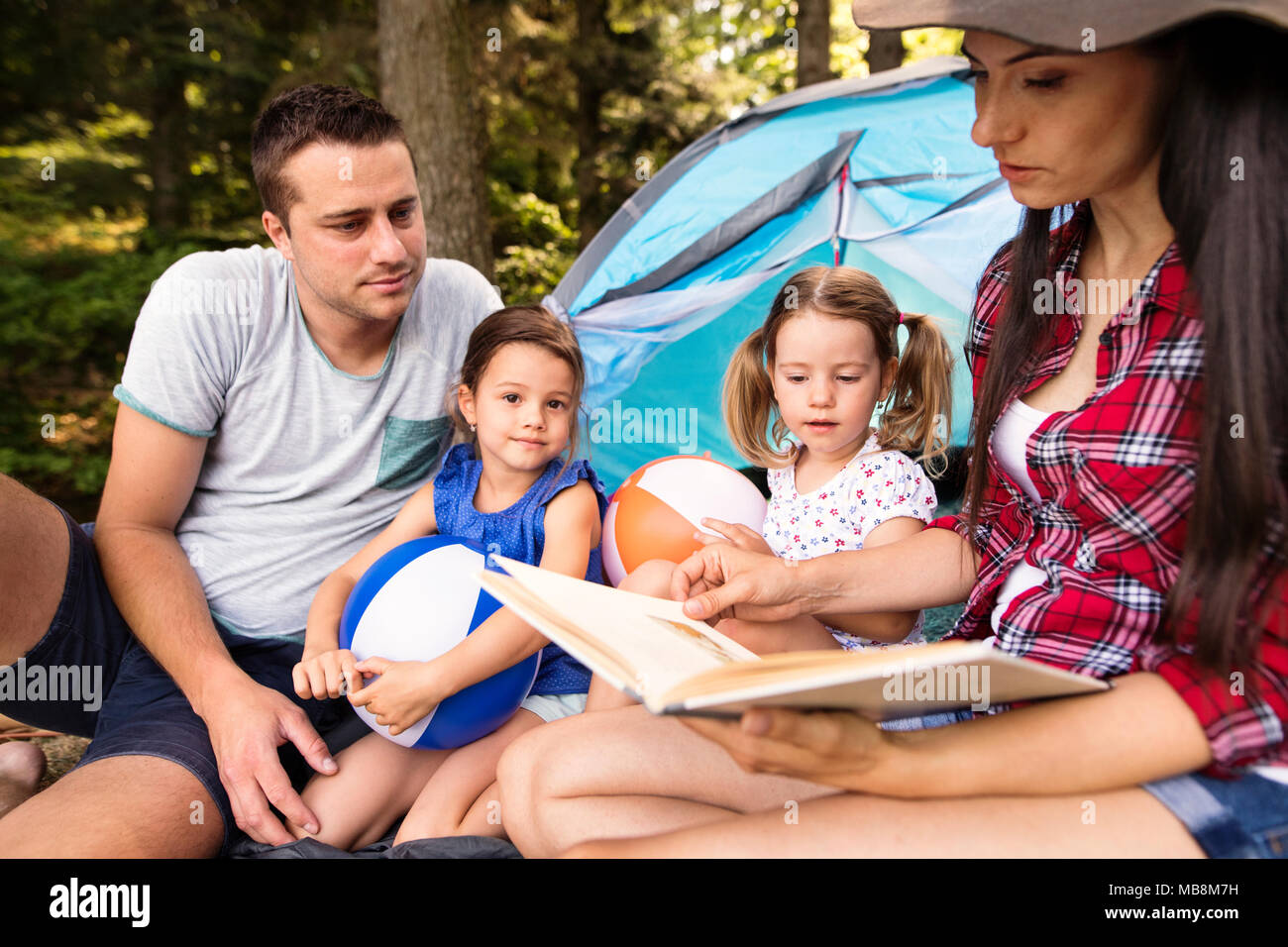 Giovane e bella famiglia con le figlie camping nella foresta. Foto Stock