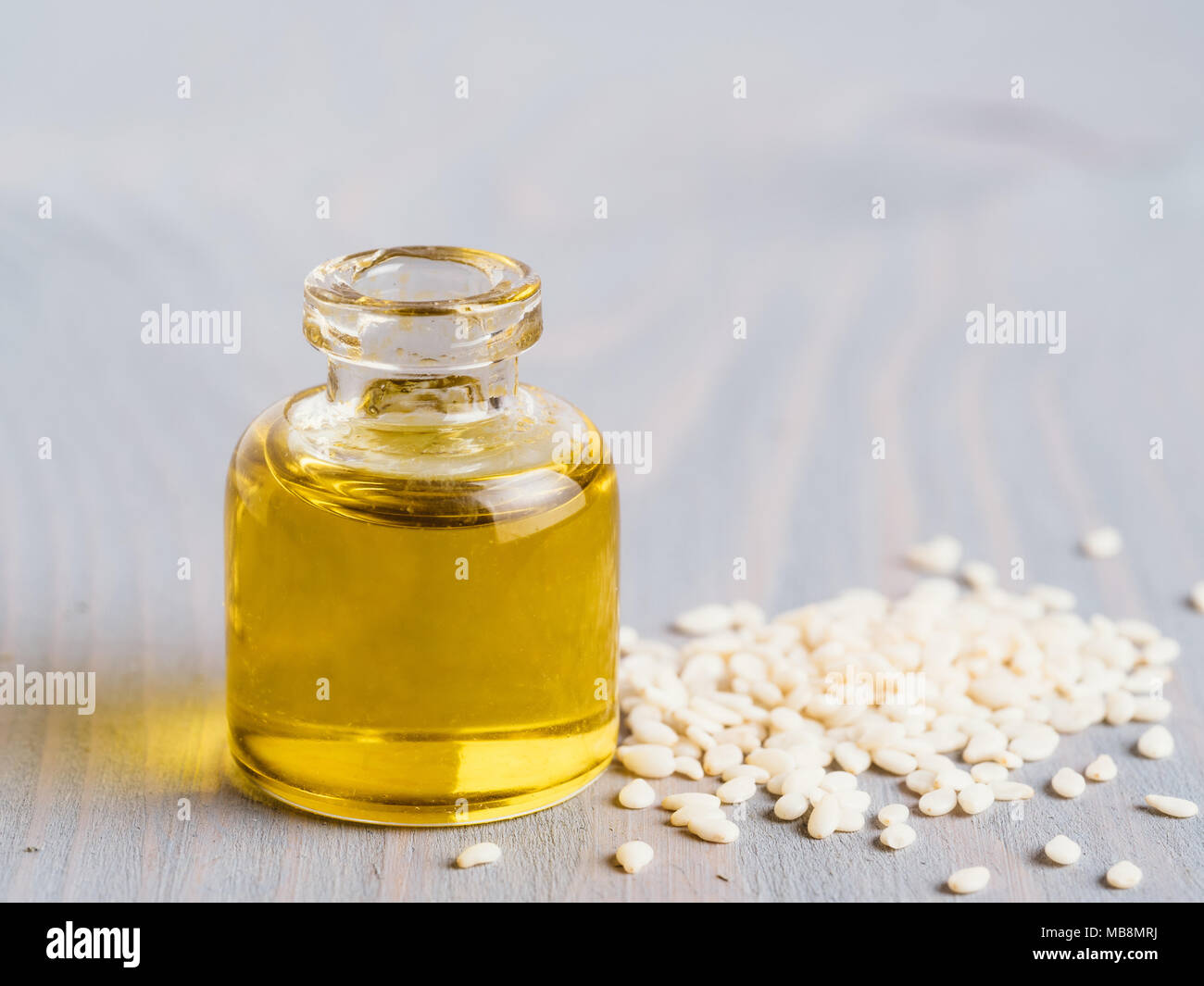 Bottiglia di olio di sesamo e i semi di sesamo sul legno grigio sfondo tabella. Copia spazio per il testo. Foto Stock